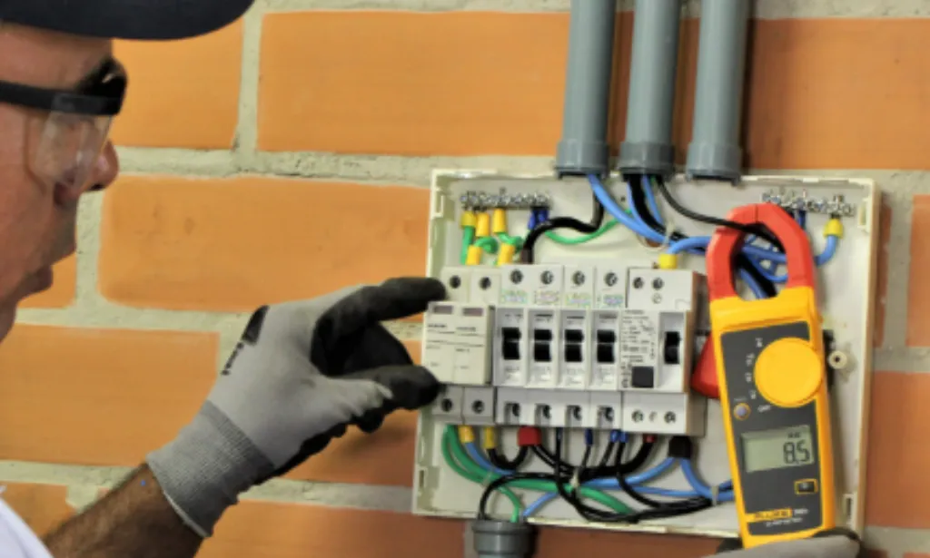 Eletricista realizando medição em quadro elétrico com alicate amperímetro